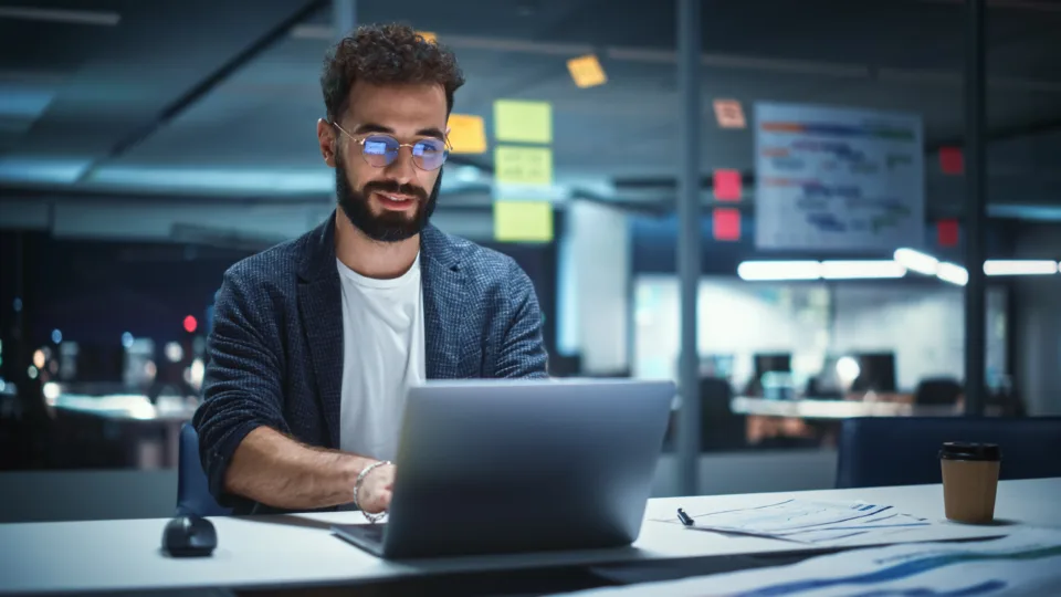 successful handsome creative director working on laptop computer in big city office late in the evening. businessman preparing for a marketing plan in conference room.